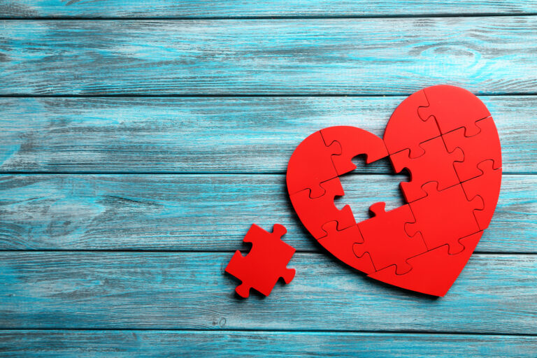 Red puzzle heart on blue wooden background - Benefits of playing games - FunFamilyGameNight.com